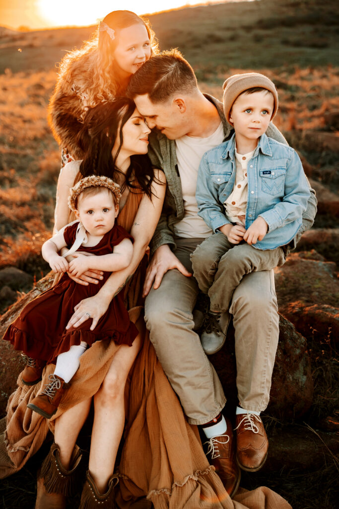 mom and dad snuggle close while hugging their children in the sunset