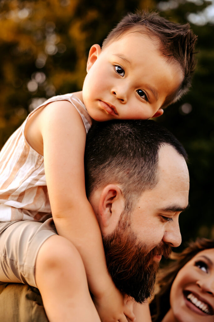 Boy sitting on father's shoulders and rests his head on father's head