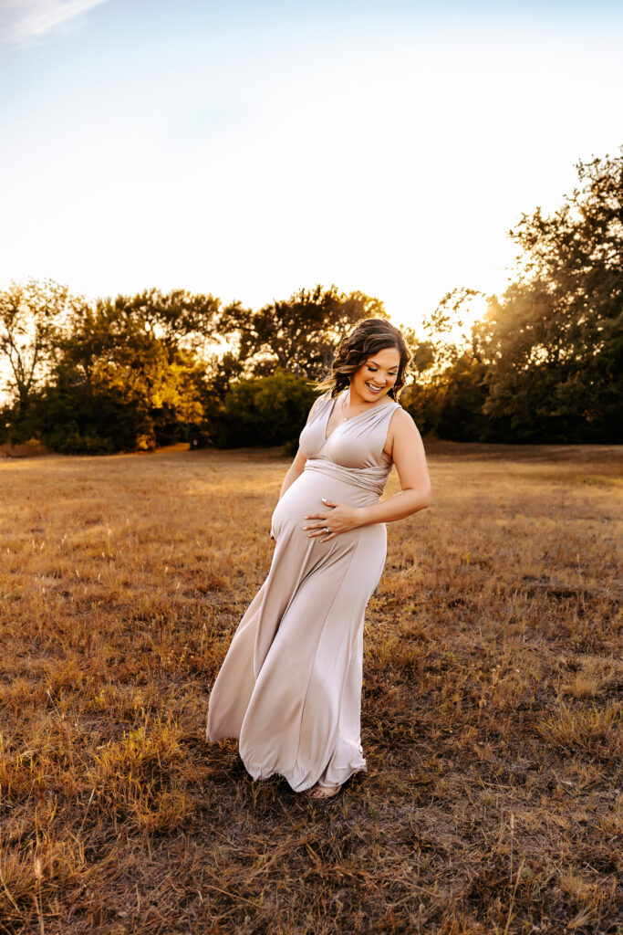 Woman laughing and holding bump during sunset maternity session