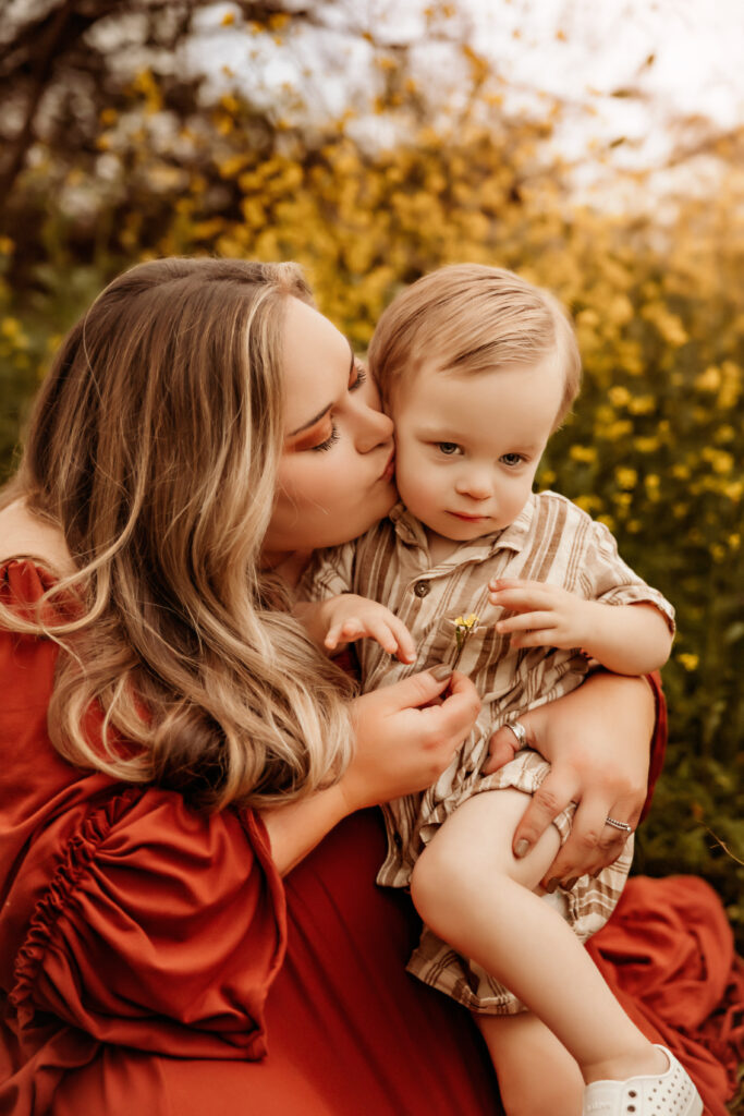 mom kissing baby boy in yellow wildflowers