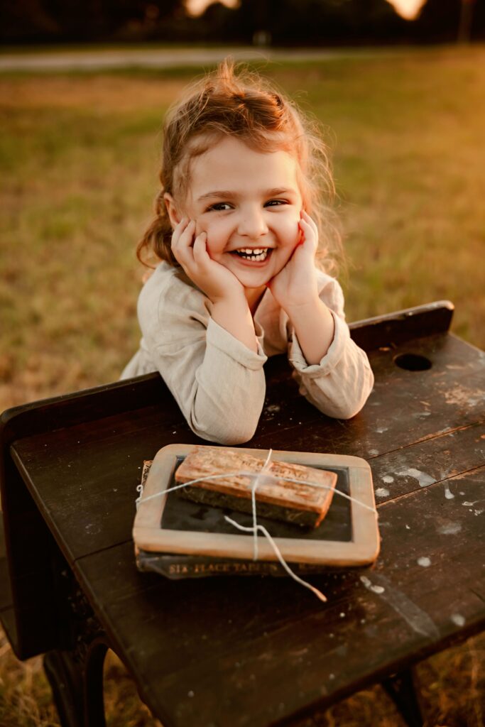Child smiling while sitting on a vintage school desk at sunset Fort Worth mini session